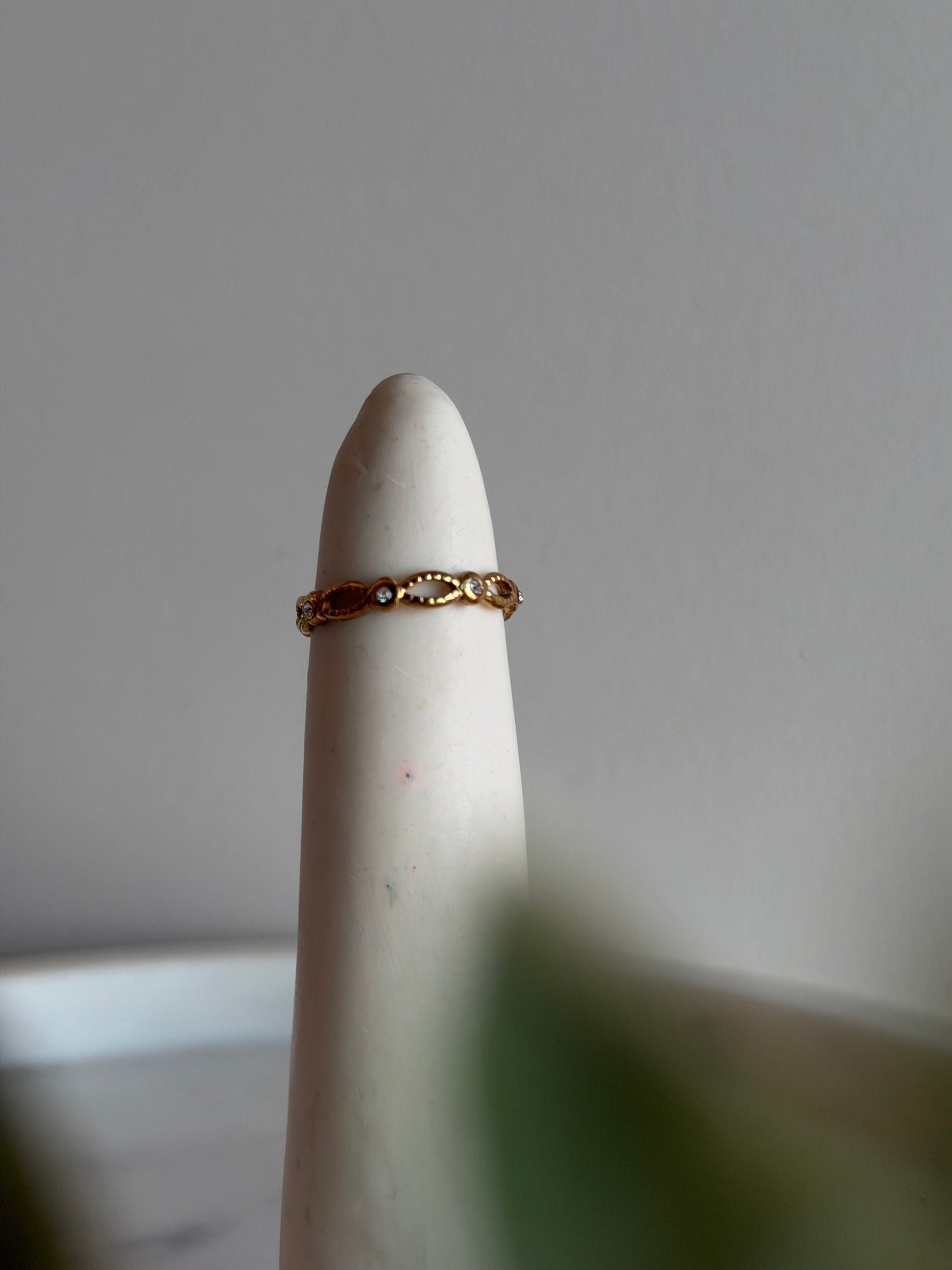 Gold ring on a white finger against a neutral background